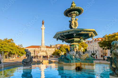 The monumental 19th century bronze fountain of four children with mermaids below, with the Column of Pedro IV behind, in Rossio Square, Lisbon, Portugal. photo