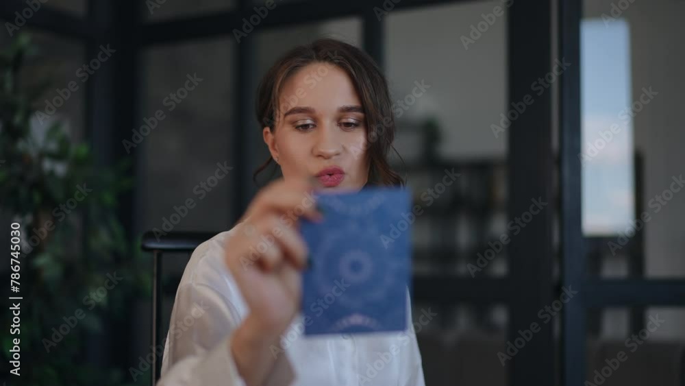 A female astrologer takes a tarot card from the table and reads what is written on the back while sitting at her desk in her office. The woman smiles while looking at the camera. Close-up A female astrologer takes a tarot card from the table and reads what is written on the back while sitting at her desk in her office. The woman smiles while looking at the camera. Close-up