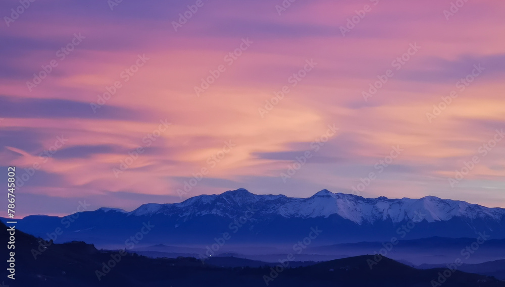 Tramonto luminoso viola arancio e rosa sopra le montagne innevate