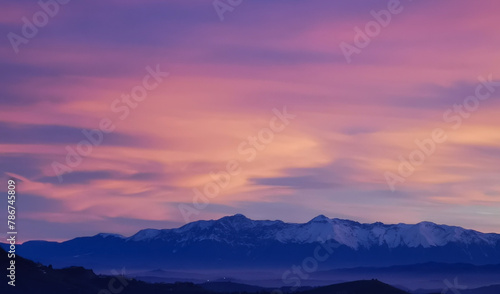 Tramonto luminoso viola arancio e rosa sopra le montagne innevate photo