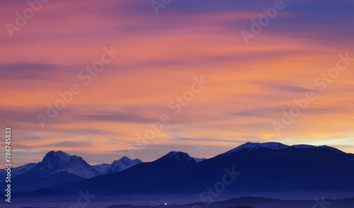 Tramonto luminoso viola arancio e rosa sopra le montagne innevate © GjGj