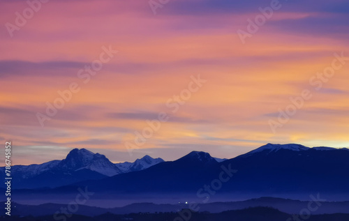 Tramonto luminoso viola arancio e rosa sopra le montagne innevate