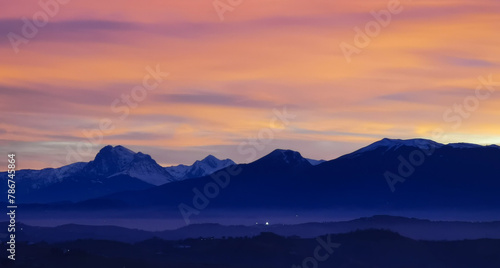 Tramonto luminoso viola arancio e rosa sopra le montagne innevate