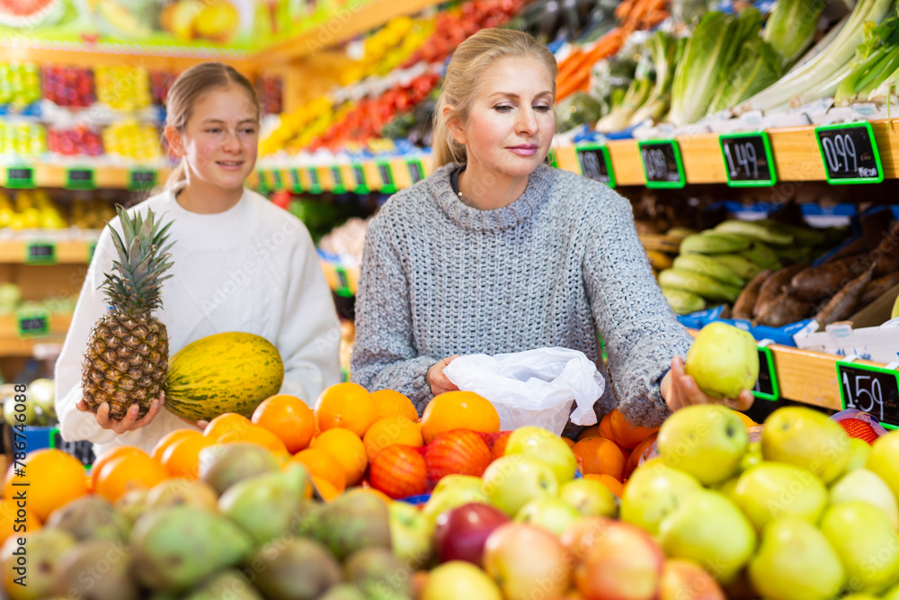 Daughter and mom buy fruit - pineapple and melon at the grocery store