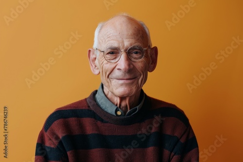 Portrait of a senior man with glasses and a striped sweater on a yellow background