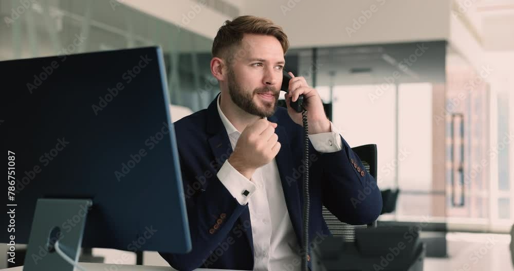 Millennial businessman, office employee sitting at workplace desk with PC holds telephone handset, answers incoming calls from company clients, provide professional help, information, support remotely