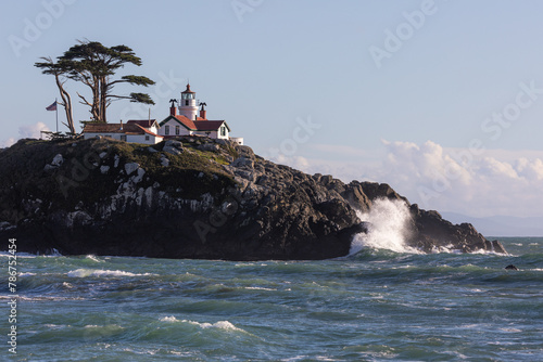 A lighthouse sits on a rocky hillside. The lighthouse is white and red, and it is surrounded by a lush green hillside. The scene is peaceful and serene. Battery Point Lighthouse, California. © wollertz