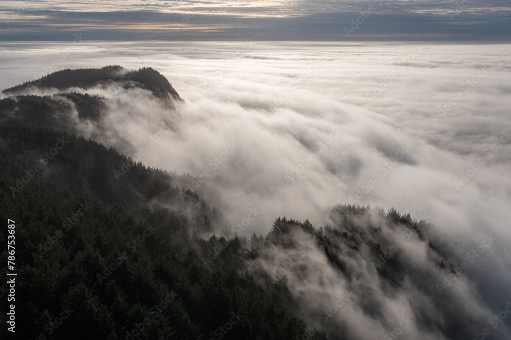 The sky is covered in a thick layer of fog, creating a moody and mysterious atmosphere. The misty clouds hang low over the mountains, giving the scene a sense of depth and grandeur