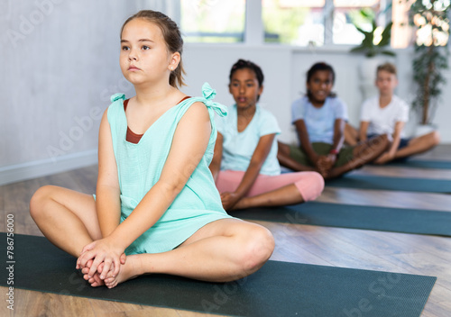 Kids stretching backs on yoga mats in sports club in Bhardrasana's pose or butterfly pose.