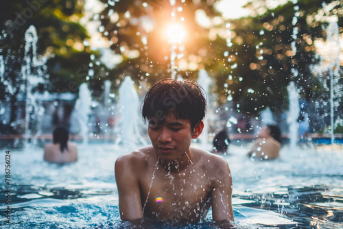 Heat exhausted young man cooling with splashes of water in fountain in extreme heat, heatwave