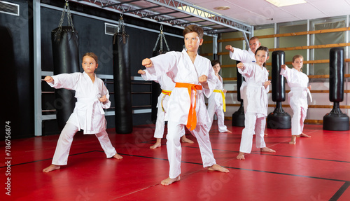 Group of preteen boys and girls doing karate kicks with male coach during karate class