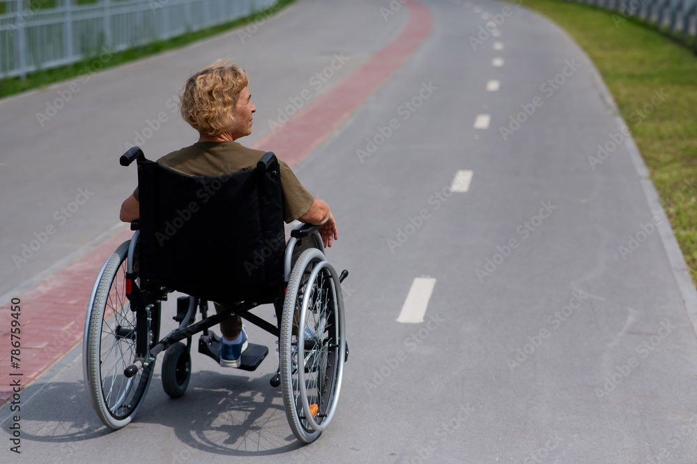 Rear view of an elderly woman in a wheelchair riding on a bike path. 