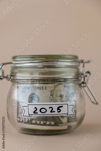 Saving Money In Glass Jar filled with Dollars banknotes. 2025 year transcription in front of jar. Managing personal finances extra income for future insecurity