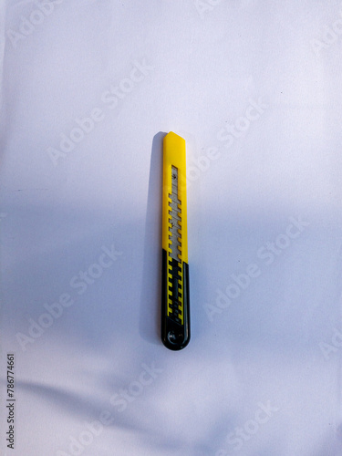 yellow and black paper cutter knife, small knife, blade, exacto knife, paper cutter on white background, dappled sunlight photo