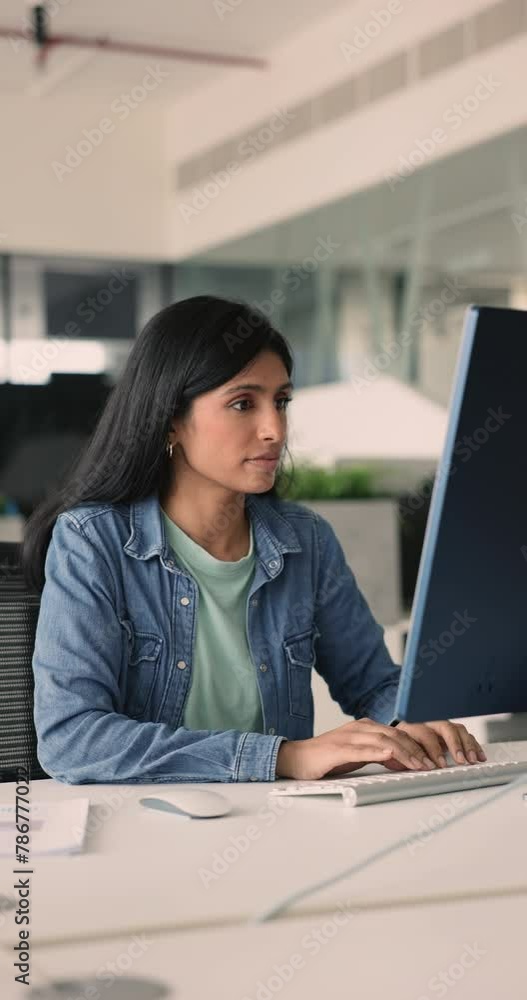 Smiling satisfied Indian business woman typing on PC keyboard seated at desk in workplace, vertical view. Corporate office employee prepare report, make research or data analysis using modern computer Smiling satisfied Indian business woman typing on PC keyboard seated at desk in workplace, vertical view. Corporate office employee prepare report, make research or data analysis using modern computer