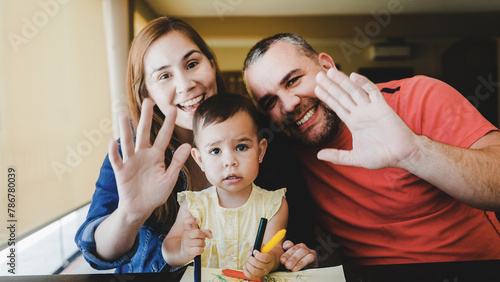 Happy family smiling on camera at home. POV Mother, baby child and father doing video call waving together.