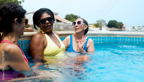 Multiracial senior women enjoy swimming pool party during summer vacations. Happy older friends having fun during travel holidays