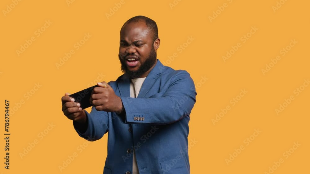 African american man playing videogames on cellphone in landscape mode, enjoying leisure time. Gamer enjoying game on mobile phone, having fun, studio background, camera A African american man playing videogames on cellphone in landscape mode, enjoying leisure time. Gamer enjoying game on mobile phone, having fun, studio background, camera A