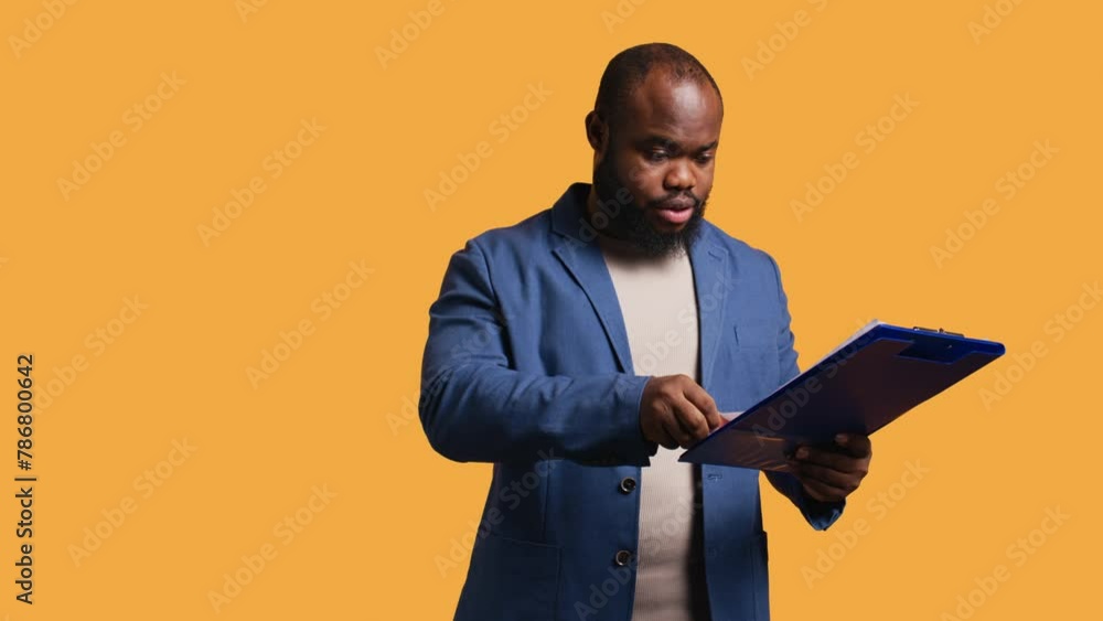 Man browsing though financial audit report on clipboard, pleased by high income, studio background. Happy african american worker reading paperwork on notepad, satisfied by figures, camera B Man browsing though financial audit report on clipboard, pleased by high income, studio background. Happy african american worker reading paperwork on notepad, satisfied by figures, camera B