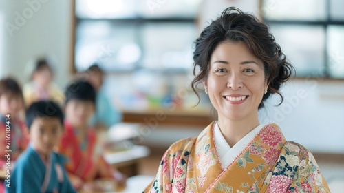 Japanese female teacher smiling at the camera, wearing a traditional kimono with floral patterns, standing inside a vibrant classroom filled with kids sitting on colorful chairs.