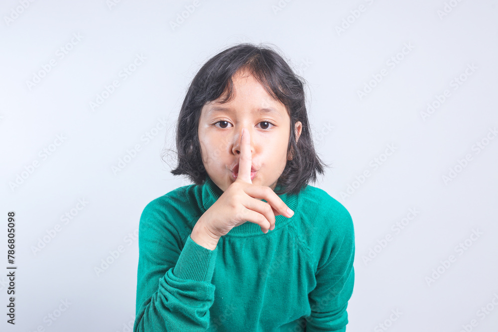 Beautiful Asian little girl putting finger up to lips and ask silence on yellow background Beautiful Asian little girl putting finger up to lips and ask silence on yellow background