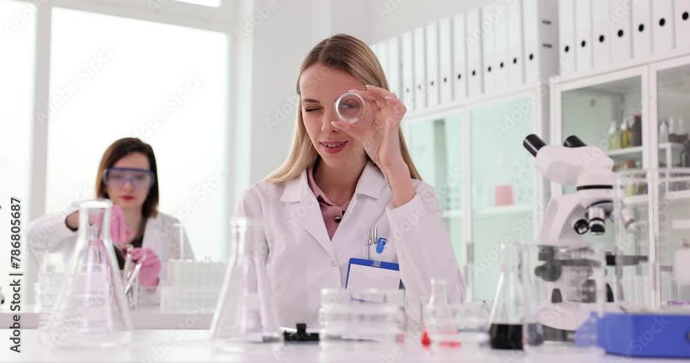 Woman looks through jar against scientist working with chemicals Woman looks through jar against scientist working with chemicals