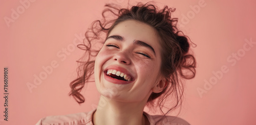 Close-up of a cheerful young woman laughing heartily against a pink background photo