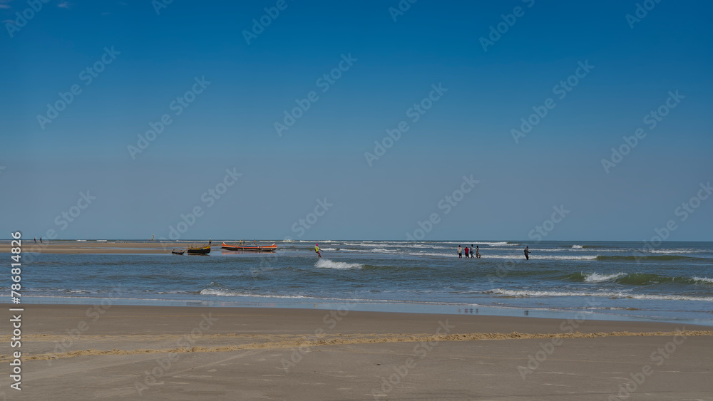 A team of fishermen at work. A group of people pulls a fishing net out of the ocean. The waves are foaming, spreading over the beach. Reflection on wet sand. Wooden pirogue boats are moored.Madagascar A team of fishermen at work. A group of people pulls a fishing net out of the ocean. The waves are foaming, spreading over the beach. Reflection on wet sand. Wooden pirogue boats are moored.Madagascar