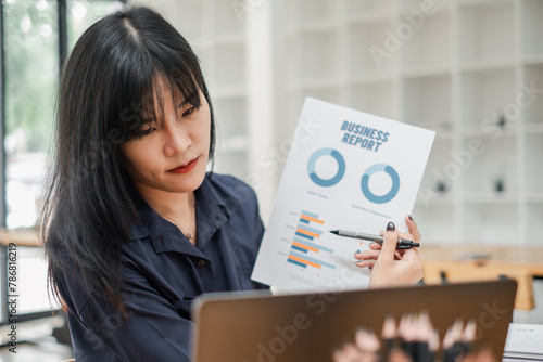 Businesswoman in a navy blue shirt examining a business report with charts, seated in front of a laptop.