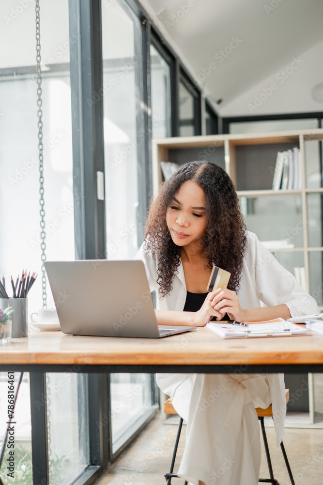 Businesswoman holding a credit card and looking at a laptop screen, possibly making an online transaction. Businesswoman holding a credit card and looking at a laptop screen, possibly making an online transaction.