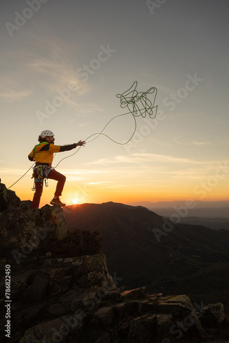 A man is standing on a mountain top with a kite in his hand. The sky is orange and the sun is setting