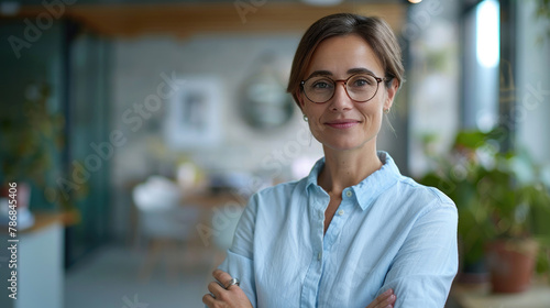 Beautiful short-haired business woman manager wearing blue shirt and glasses standing in modern office with folded hands and smiling at the camera © boxstock production