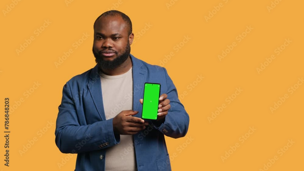 Upset african american man showing thumbs down sign gesturing holding green screen phone, disapproving. BIPOC person doing rejection hand gesture regarding smartphone, studio background, camera A Upset african american man showing thumbs down sign gesturing holding green screen phone, disapproving. BIPOC person doing rejection hand gesture regarding smartphone, studio background, camera A