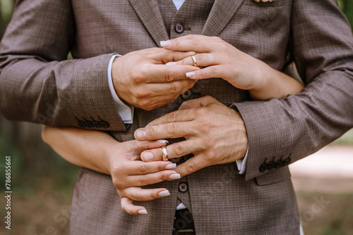 Valmiera, Latvia- July 28, 2024 - A close-up of a newlywed couple's hands, showcasing their wedding rings, with the groom embracing the bride from behind.