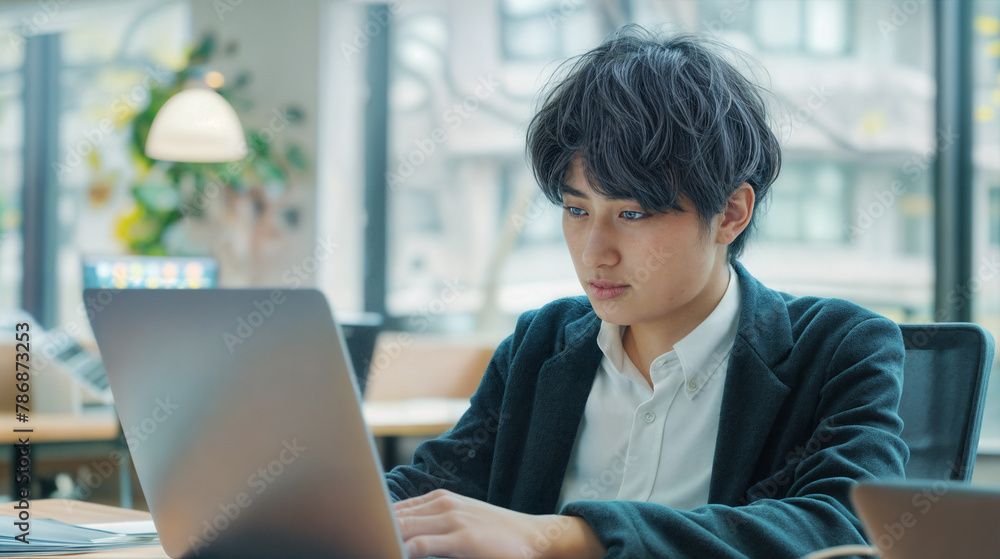 A young asian man works on a computer while sitting at a table in a modern bright office A young asian man works on a computer while sitting at a table in a modern bright office