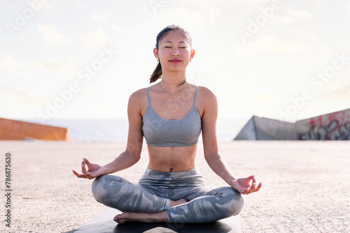 young asian woman doing meditation by the sea sitting on a yoga mat, concept of mental relaxation and healthy lifestyle
