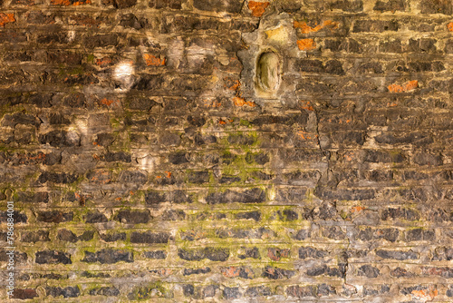 Close-up view of an old weathered brick wall with moss growth adding a touch of green