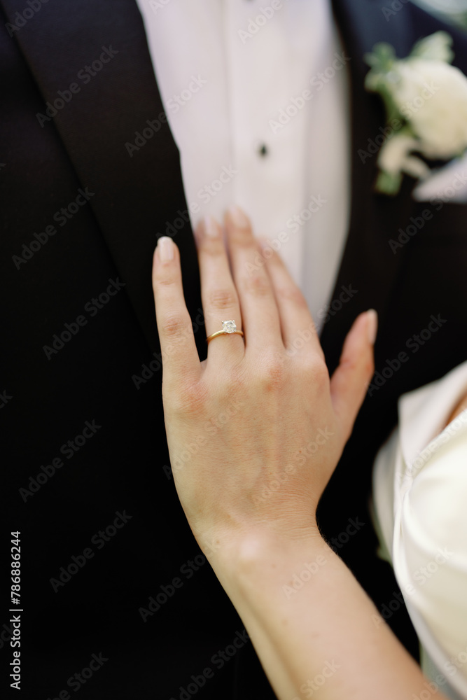 Bride's hand with engagement ring against groom's suit