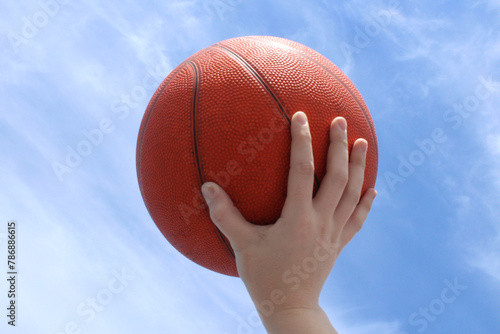 Hand holding basketball against a clear blue sky