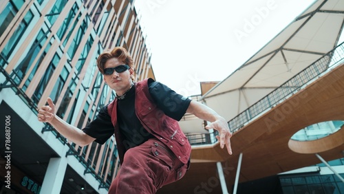 Low angle of asian attractive hipster pose at camera surround by mall. Portrait of break dance choreographer looking at camera while dancing in hip hop style. Outdoor sport 2024. Endeavor.