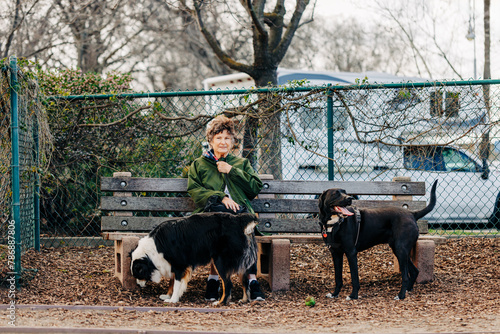 Woman sitting on bench at dog park with two dog on windy day