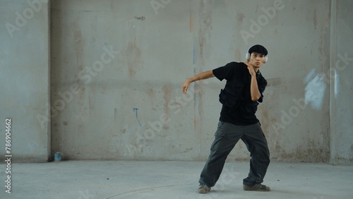 Handsome hipster practicing break dancing while listening music from headphone with cement background. Motion shot of street dancer perform robot dance. Outdoor sport 2024. Modern dance. Endeavor. © Summit Art Creations