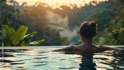 A woman relaxing in an infinity pool enjoying the natural scenery of lush greenery and trees at sunset, feeling calm after her spa experience © Kien