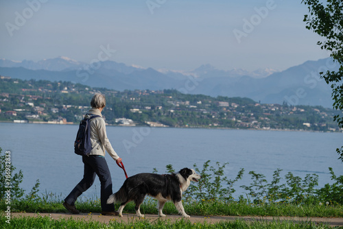 Woman with a dog walking in motion in the background Lake Garda, mountain peaks in the snow.