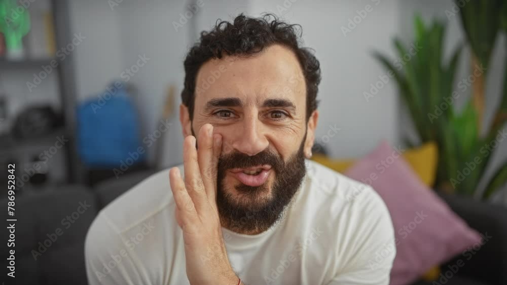 Middle-aged man, handsome with beard, wearing white t-shirt whispering a devious secret, hand covering mouth in indoor chatter. spicy living room talk at home! Middle-aged man, handsome with beard, wearing white t-shirt whispering a devious secret, hand covering mouth in indoor chatter. spicy living room talk at home!