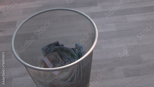 Throwing wad of dollar bills on the paper trash can, wooden floor background.