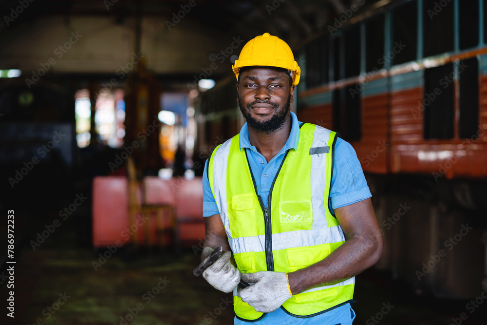 A man in a yellow vest and a hard hat is standing in a train station. He is smiling and looking at the camera A man in a yellow vest and a hard hat is standing in a train station. He is smiling and looking at the camera