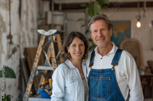 A caucasian couple is smiling at the camera, one man in overalls with a tool box and ladder in the background. Retro scene. Family photograph. An intimate moment captured at home with a middle-aged © MD Media