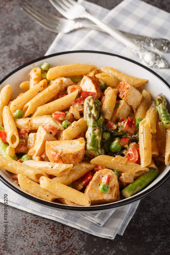 Spicy Chicken Chipotle Pasta with asparagus, bell pepper, green pea and onion closeup in the bowl on the table. Vertical