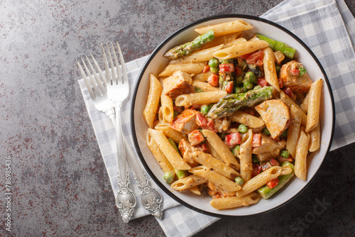 Hot chicken pasta with asparagus, bell peppers and green peas in a creamy chipotle cheese sauce closeup in the bowl on the table. Horizontal top view from above photo